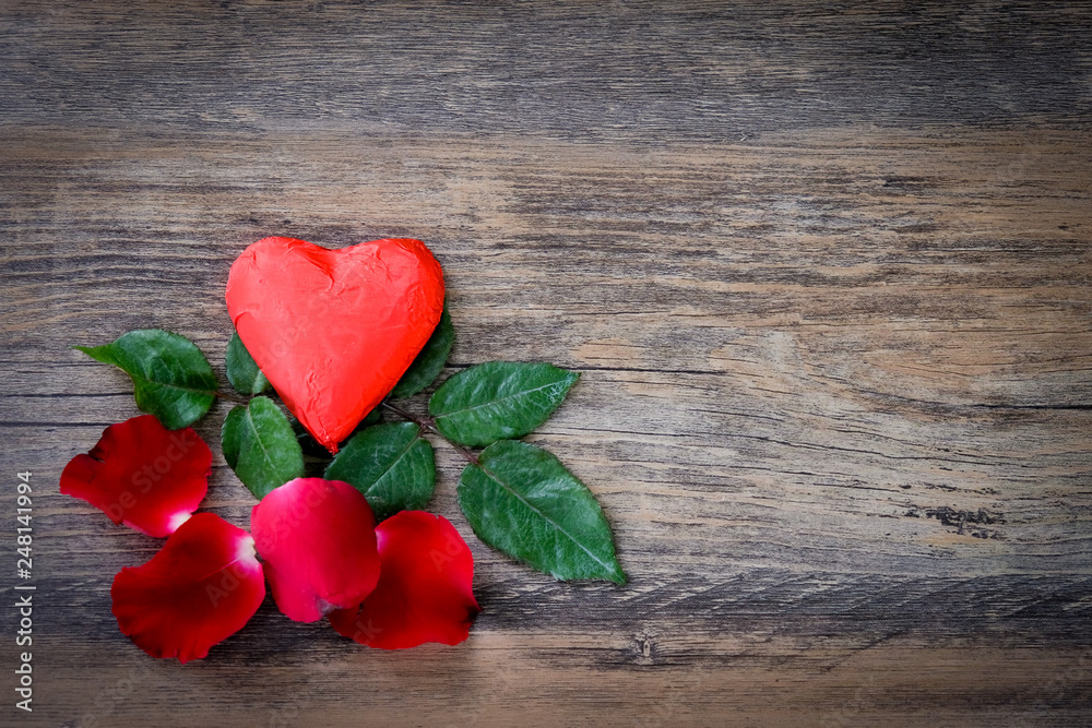 Heart shaped chocolate candy with red wrappings and red rose on wood background Heart shaped chocolate candy with red wrappings and red rose on wood background