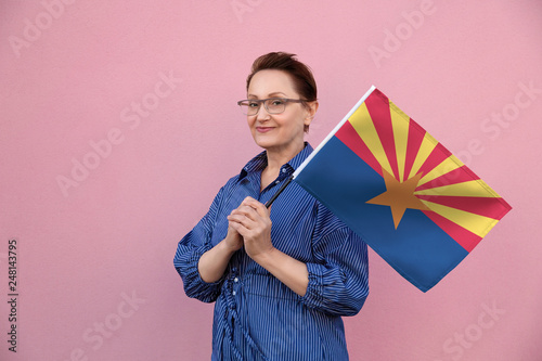 Arizona flag. Woman holding Arizona state flag. Nice portrait of middle aged lady 40 50 years old holding a large state flag over pink wall background on the street outdoor. photo