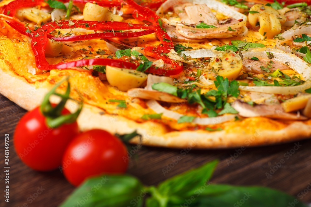 Close up Italian pizza with melted cheese, red tomatoes, pepper, mushrooms, onion and herbs on a brown table decorated by cherry tomatoes and fresh green basil leaves Close up Italian pizza with melted cheese, red tomatoes, pepper, mushrooms, onion and herbs on a brown table decorated by cherry tomatoes and fresh green basil leaves