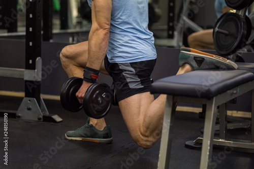 Attractive man doing lunges step-ups with heavy dumbbell.