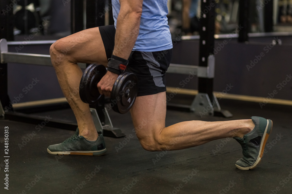 Attractive man doing lunges step-ups with heavy dumbbell.