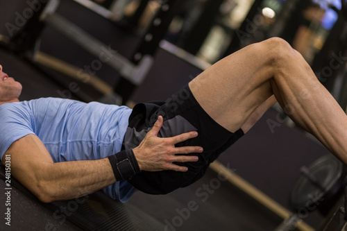 Image of a muscular man using a bench to make abdominal exercise at the gym.