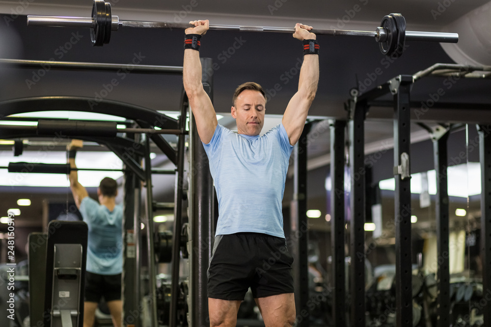 Muscular man holding barbell above the head at the gym. Muscular man holding barbell above the head at the gym.