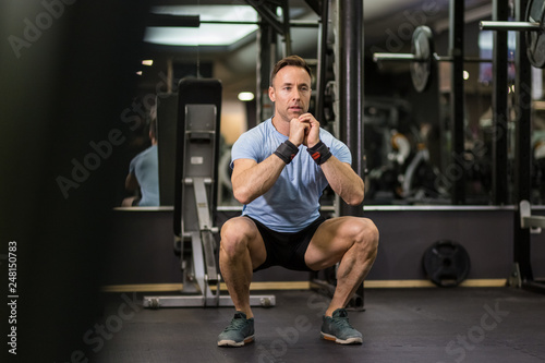 Image of a muscular man doing squads at the gym.