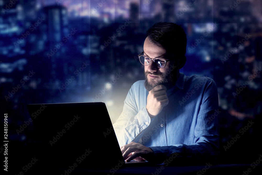 Young handsome businessman working late at night in the office with blue lights in the background Young handsome businessman working late at night in the office with blue lights in the background