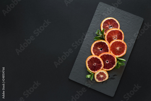 Fresh blood orange slices decorated mint leaves on dark slate background. Top view. Copy space