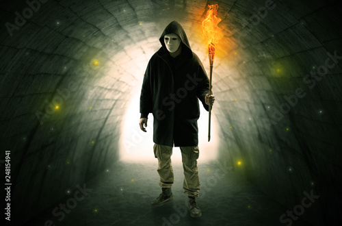 Ugly man with burning flambeau walking in a dark tunnel