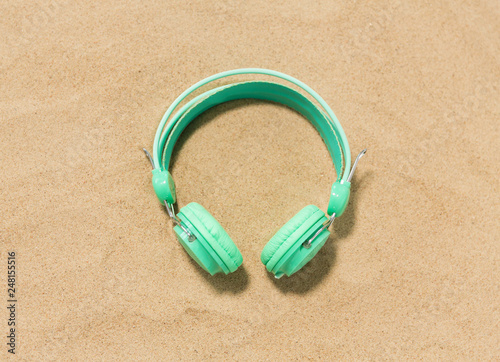 music, audio equipment and vacation concept - earphones on summer beach sand