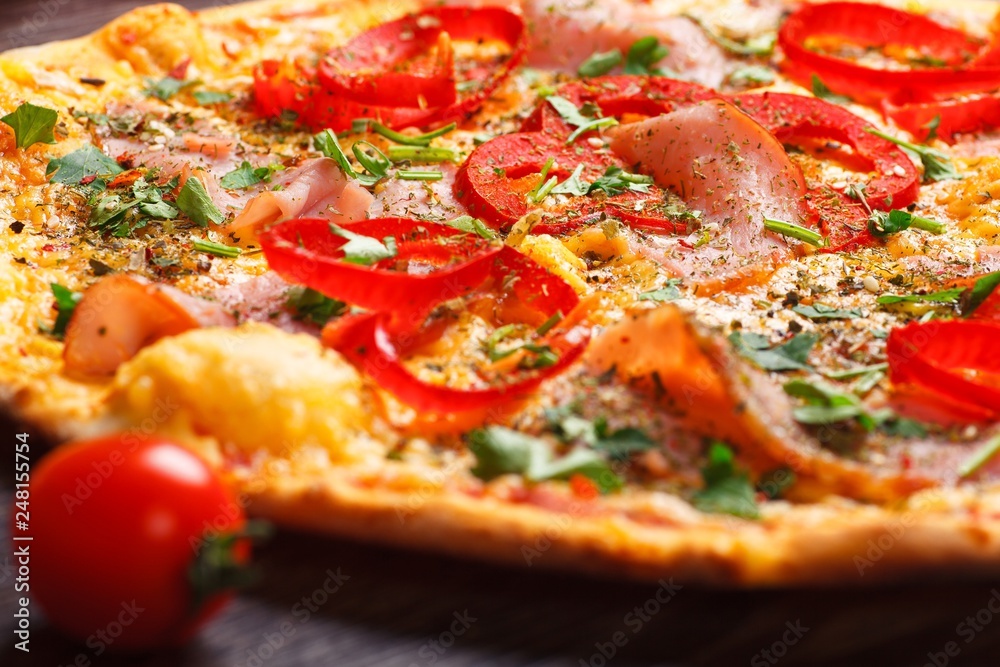 Close up Italian pizza with ham, cheese, pepper and herbs on a brown table decorated by mushrooms, red sweet pepper and cherry tomatoes Close up Italian pizza with ham, cheese, pepper and herbs on a brown table decorated by mushrooms, red sweet pepper and cherry tomatoes
