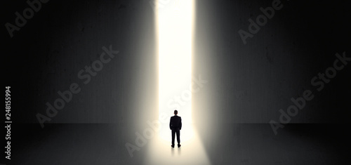Businessman standing and seeing the light at the end of a big wall
