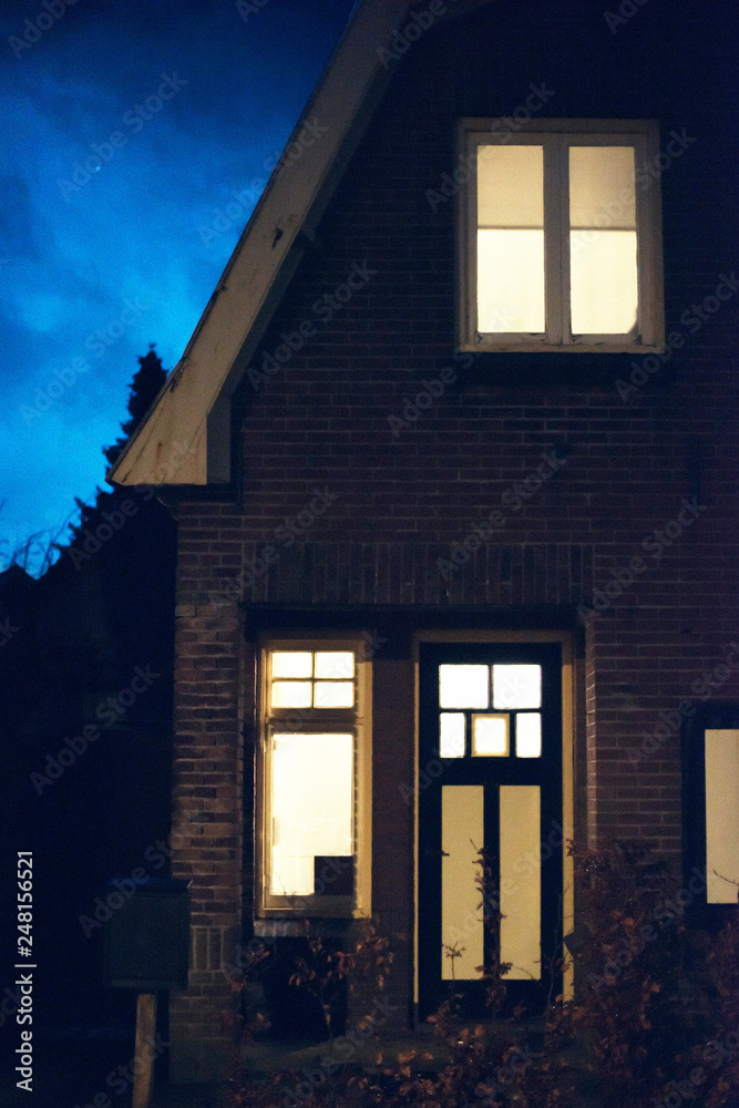 Illuminated windows and front door of house at dusk.