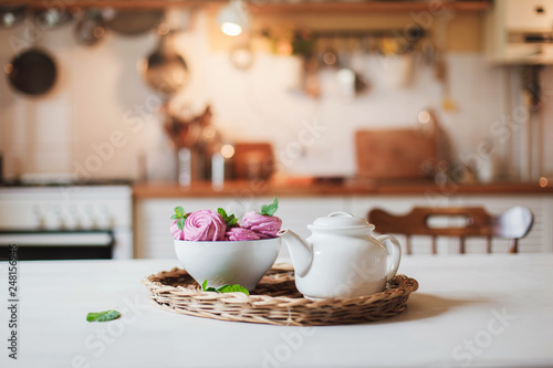 Wallpaper Mural White teapot and pink cupcakes are serving on straw wicker tray on table. Tea time, cozy home atmosphere hygge. Kitchen still life in warm light. Sweets with mint herbal leaves. Torontodigital.ca