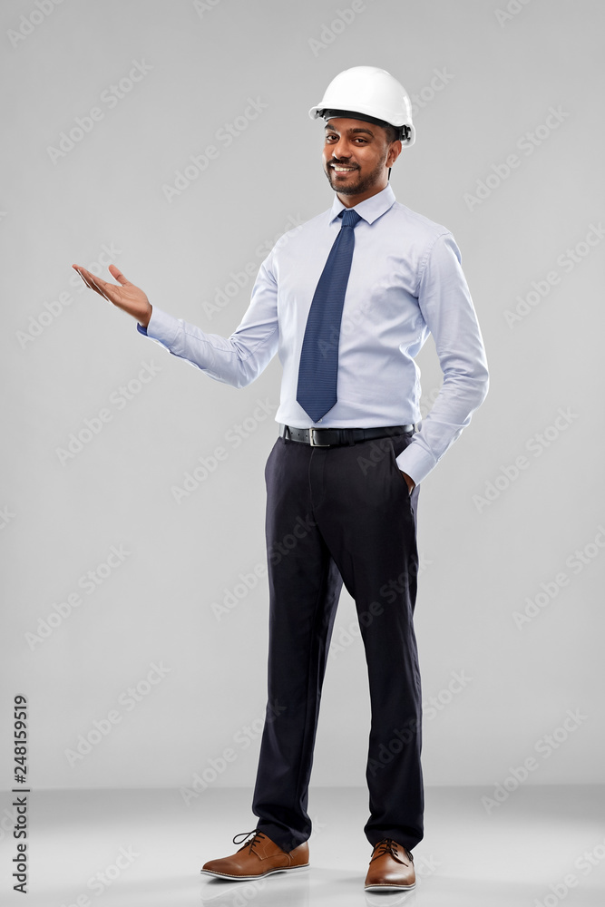 architecture, construction business and building - smiling indian architect or businessman in helmet showing something imaginary over grey background architecture, construction business and building - smiling indian architect or businessman in helmet showing something imaginary over grey background