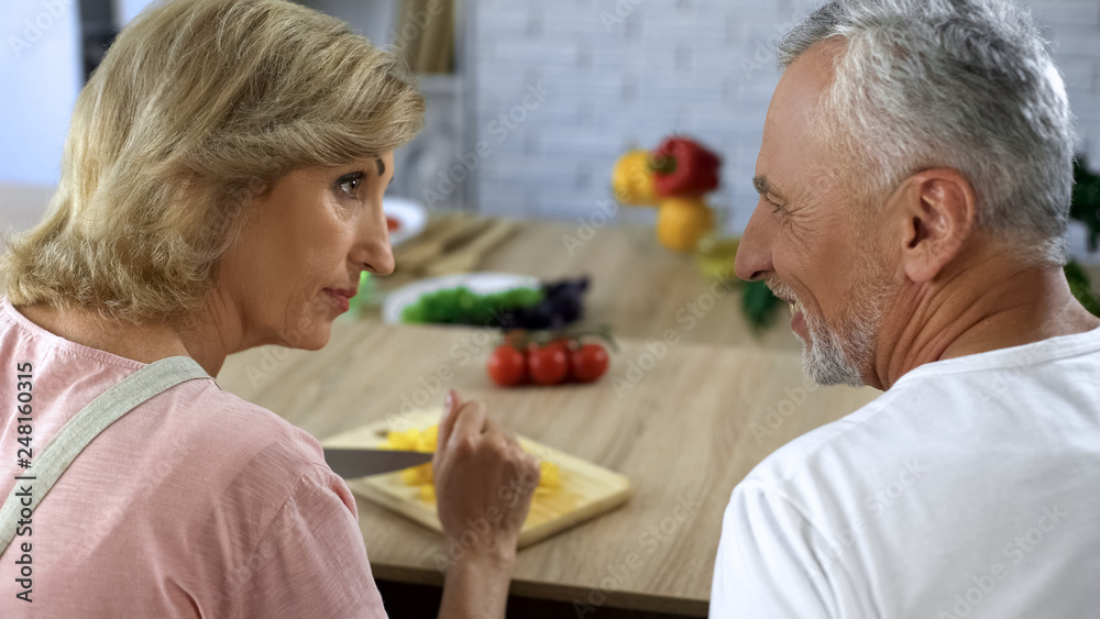 Smiling old husband looking at wife cooking dinner at home kitchen, family Smiling old husband looking at wife cooking dinner at home kitchen, family