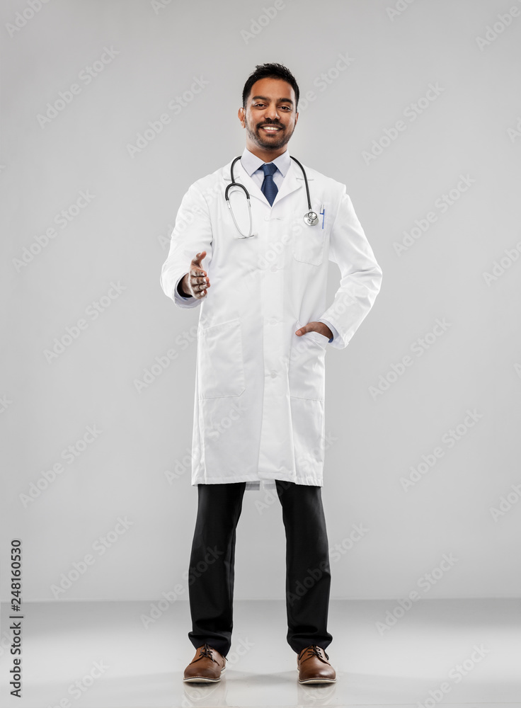 medicine, gesture and healthcare concept - smiling indian male doctor in white coat with stethoscope stretching hand for handshake over grey background medicine, gesture and healthcare concept - smiling indian male doctor in white coat with stethoscope stretching hand for handshake over grey background