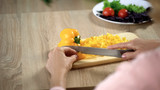 Female hands cutting fresh yellow pepper on chopping board in kitchen, cooking