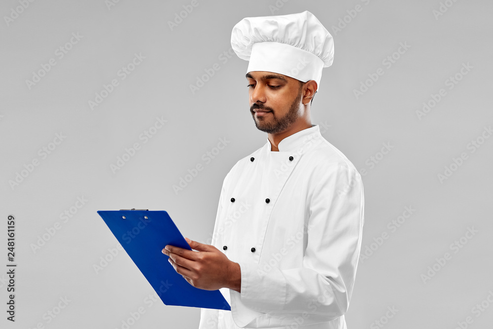 cooking, profession and people concept - male indian chef in toque reading menu on clipboard over grey background cooking, profession and people concept - male indian chef in toque reading menu on clipboard over grey background