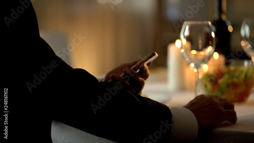 Elegant male scrolling smartphone application, waiting for date in restaurant