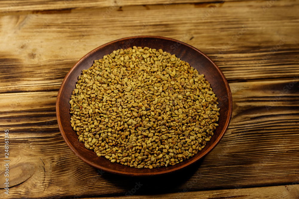 Fenugreek seeds in ceramic plate on wooden table Fenugreek seeds in ceramic plate on wooden table