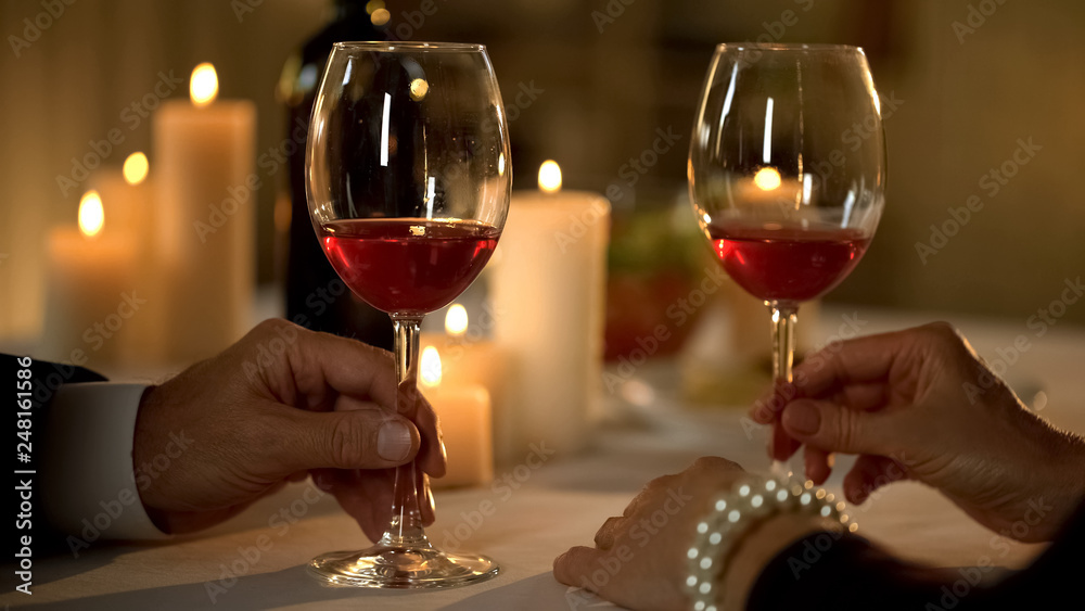 Male and female hand holding glasses with red wine on table, romantic tradition