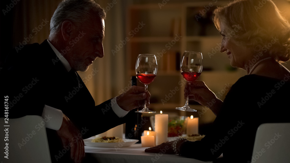 Senior male and female toasting with wine glasses, aged couple flirting on date Senior male and female toasting with wine glasses, aged couple flirting on date