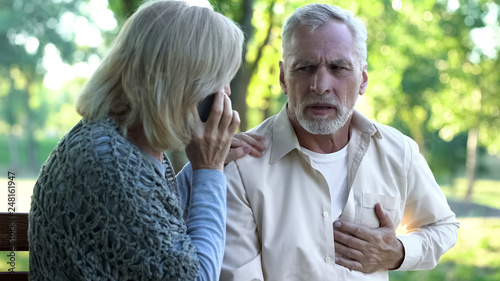 Old couple sitting on bench, man suffering arrhythmia, wife calling emergency photo