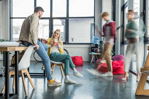 female and male casual businesspeople sitting and having discussion in loft office with colleagues in motion blur on background