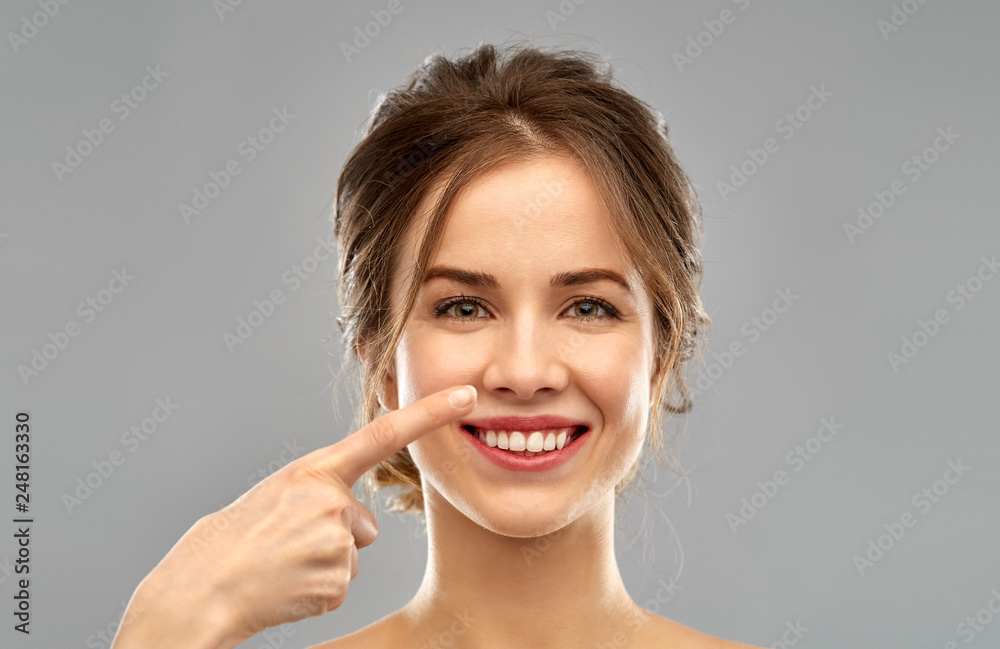 beauty, people and rhinoplasty concept - beautiful young woman pointing to her nose over grey background beauty, people and rhinoplasty concept - beautiful young woman pointing to her nose over grey background