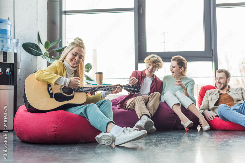 happy group of friends sitting on bean bag chairs and playing guitar