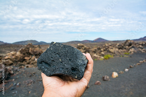 Hand holding a lava stone and a volcano in the background. photo