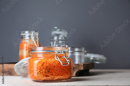 Jar with tasty fermented carrot on white table