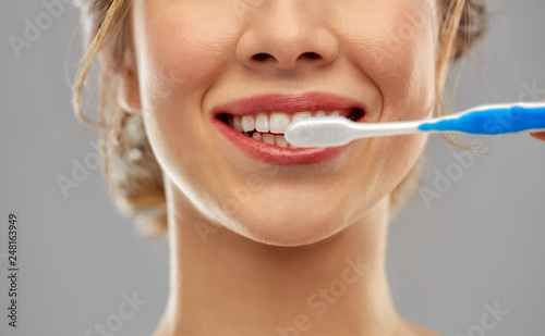 oral care, dental hygiene and people concept - close up of smiling woman with toothbrush cleaning teeth over gray background