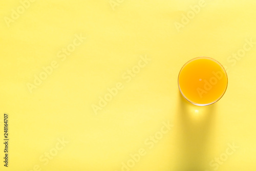 Glass of fresh juice, top view. Orange juice on yellow background.