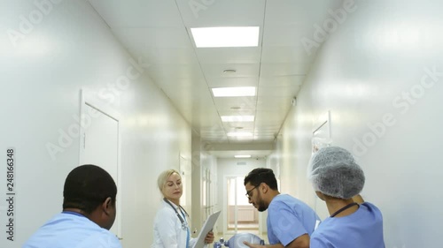 Following dolly shot with tilt down of emergency room nurses administering oxygen and IV fluids to unresponsive patient and pushing gurney as female doctor giving instructions photo