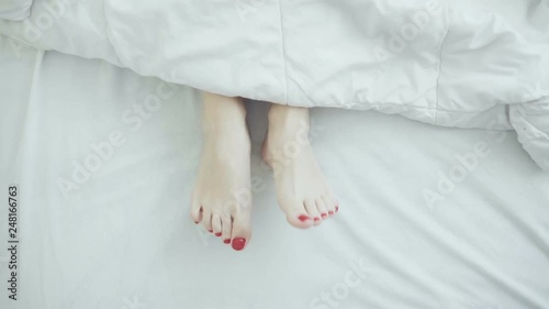 Female legs in bed view from above, white bedding, dancing