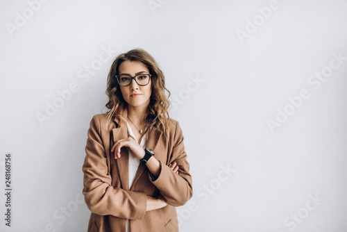 Attractive business woman stands near a white wall with a serious face. Blank space for a text photo