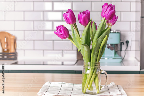 Purple tulips in a glass jar standing on the modern kitchen