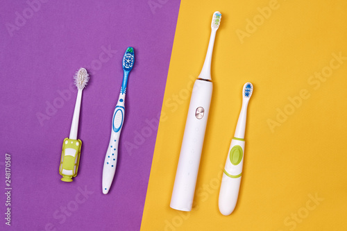 Manual and Adult and baby smart electric toothbrushes. Purple and yellow paper background. Dental care