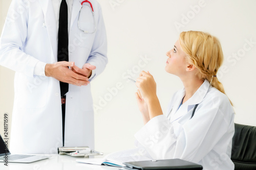 Young female doctor at hospital office having conversation talking with another male doctor standing beside the table. Concept of medical healthcare professional team. photo