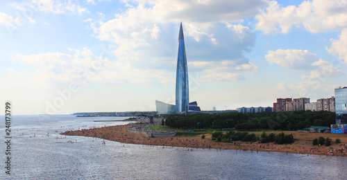 Modern Skyscraper Architecture View with Public City Beach and People Relaxing on Summer Day. Urban Tall Building in Downtown Area Facing the Park and Sandy Beach in Saint Petersburg, Russia