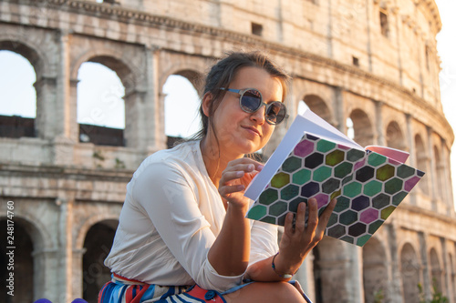 Canvas Print Beautiful young woman reading book sitting in front of colosseum in Rome at sunset