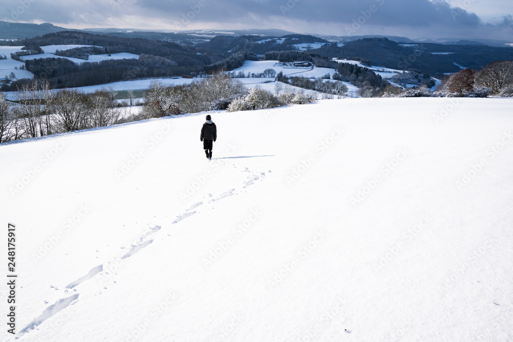 One walks in the snow with white hills in the background