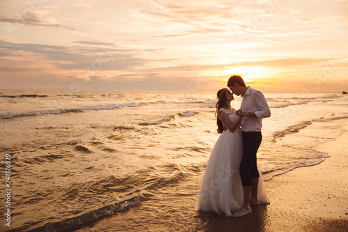 Bride and groom hugging and hold each other's hands at beautiful sunset background. Newlyweds at wedding day on ocean beach