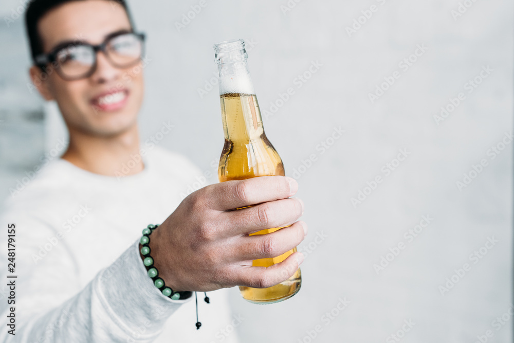 smiling mixed race man in glasses holding bottle of beer in stretched hand smiling mixed race man in glasses holding bottle of beer in stretched hand