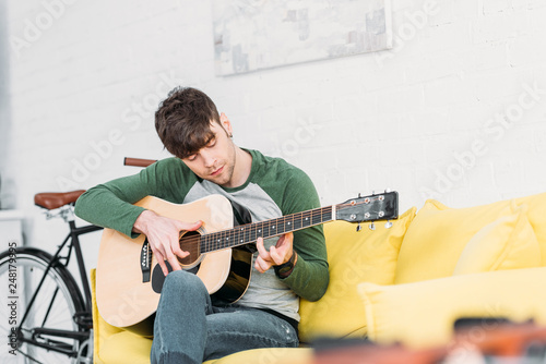 handsome young man playing acoustic guitar while sitting on yellow sofa photo