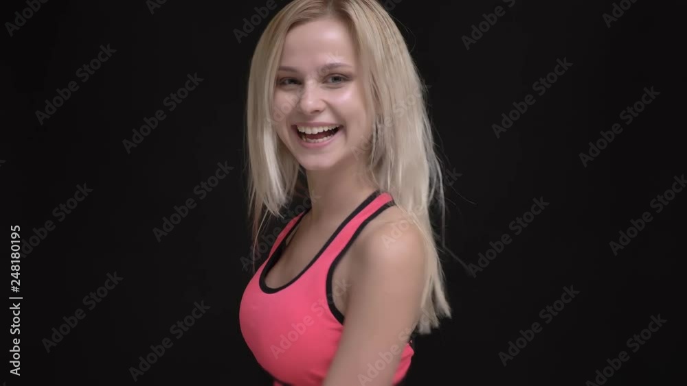 Portrait of young white-haired caucasian girl in pink jumpsuit joyfully spinning around and smiling into camera on black background. Portrait of young white-haired caucasian girl in pink jumpsuit joyfully spinning around and smiling into camera on black background.