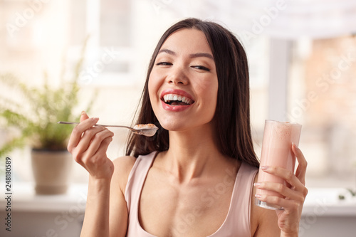 Young girl at kitchen healthy lifestyle standing with glass of shake looking camera laughing joyful