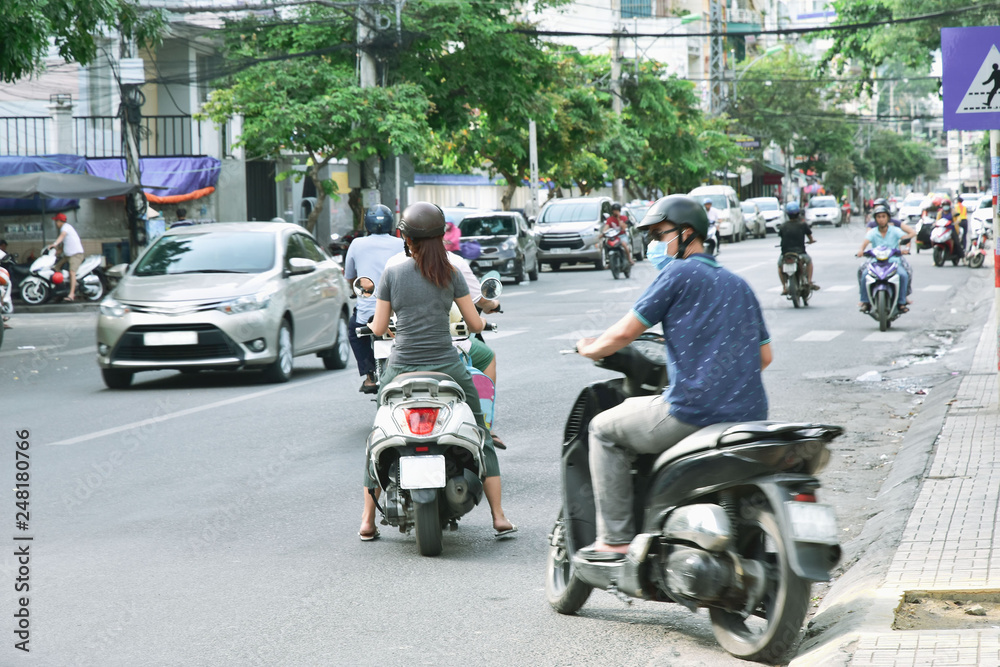 Man and woman on mopeds go out of the alley on the road. They have helmets
