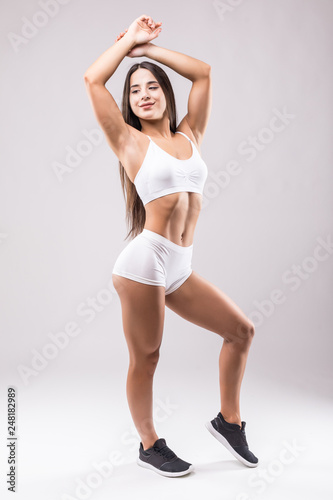 Young and sporty woman in white sportwear with perfect body standing isolated on white background