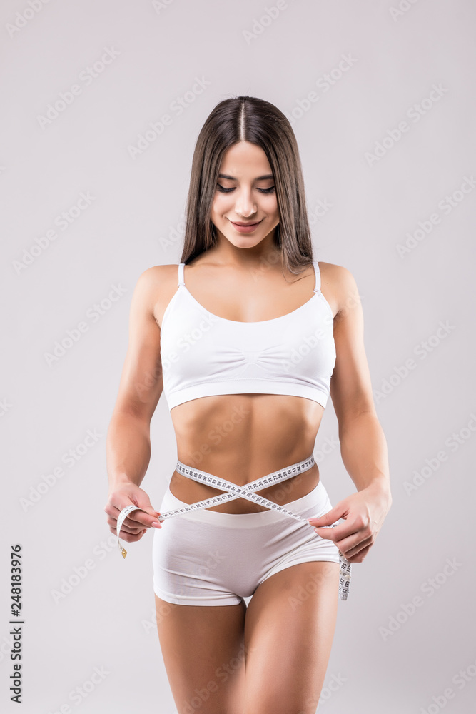 Fototapeta premium Fitness young woman taking body measurements with tape isolated over a white background
